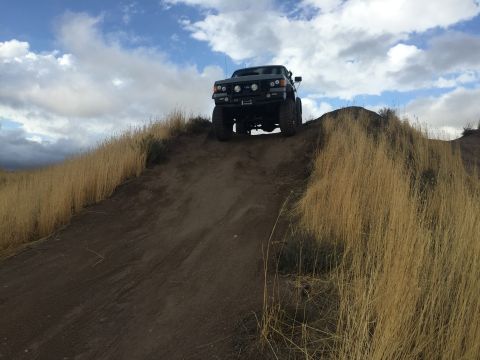 1988 Ford Bronco - SUV ascends a steep dirt incline under a cloudy sky.