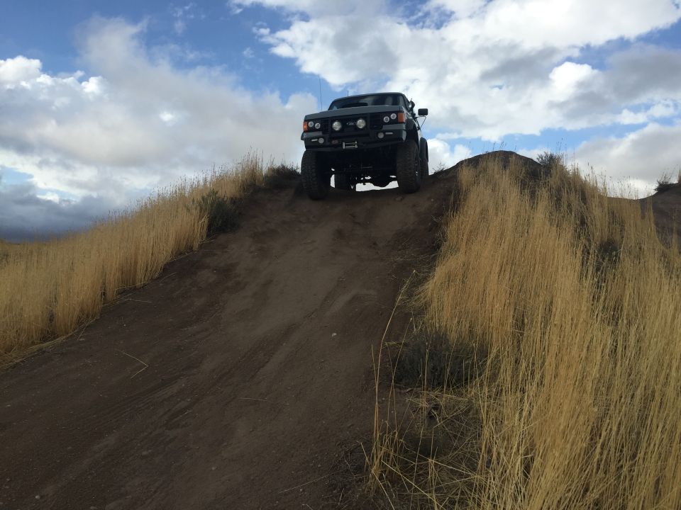 Dark SUV with winch on front bumper climbing a dirt hill, dry grass on sides