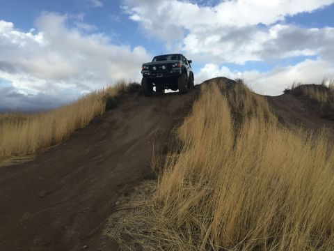 1988 Ford Bronco - A 1988 Ford Bronco navigates a steep dirt incline under a cloudy sky.