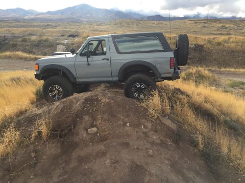 1988 Ford Bronco - This 1988 Ford Bronco is shown navigating a challenging off-road terrain with a spare tire mounted on the rear.