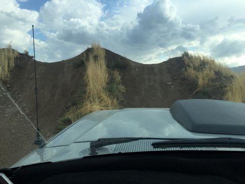 1988 Ford Bronco - View from inside a vehicle, showing the hood scoop and antenna against a backdrop of a dirt hill and sky.