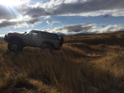1988 Ford Bronco - A gray SUV navigates a dry, grassy landscape under a dramatic sky.