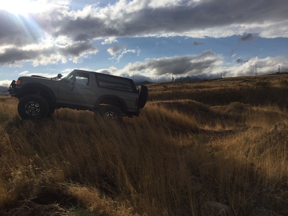 Gray SUV with off-road tires driving on a grassy hill under a cloudy sky