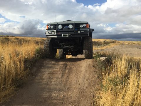 1988 Ford Bronco - This heavily modified off-road vehicle navigates a dirt track, its imposing stance and custom bumper suggesting off-road capability.