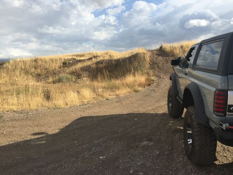 1988 Ford Bronco - Ford Bronco driving on a dirt path through a dry, grassy landscape under a cloudy sky.