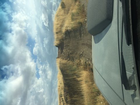 1988 Ford Bronco - A gray SUV is seen from the side, driving on a dirt road with dry grass and a cloudy sky.