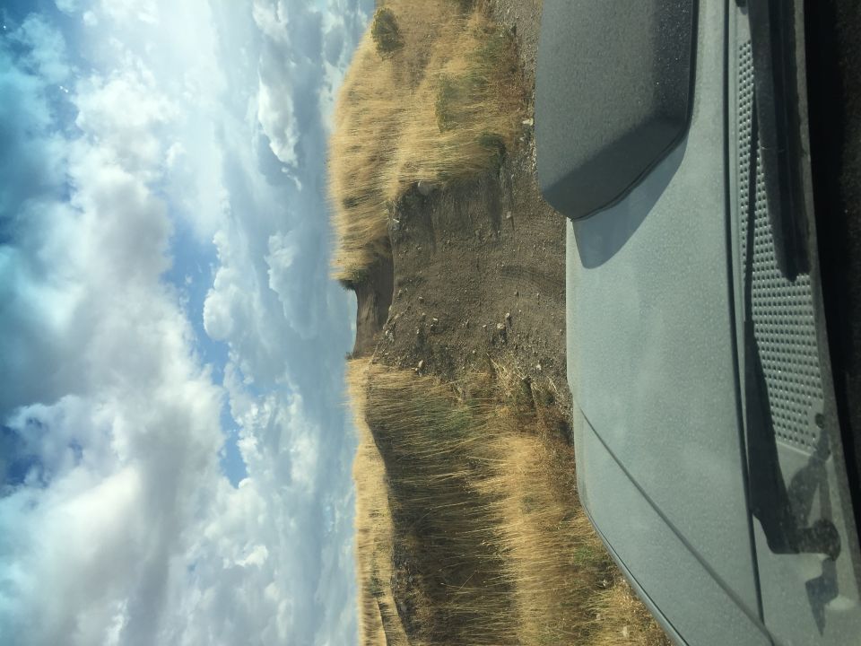Gray SUV side panel and fender against a cloudy sky and dry grass hillside