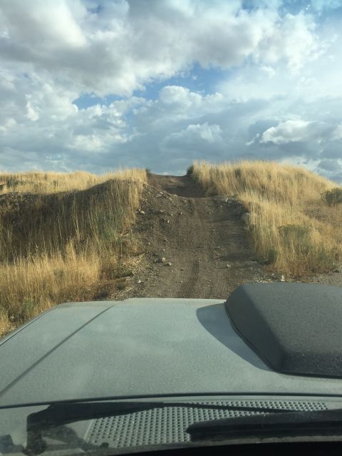 1988 Ford Bronco - Driving up a steep dirt path with dry grass lining the sides under a cloudy sky.