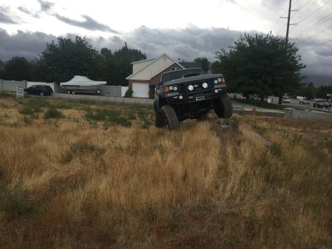 1988 Ford Bronco - A heavily modified SUV is shown navigating a steep, grassy embankment under a cloudy sky.