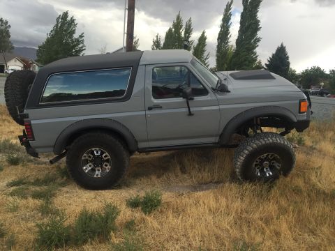 1988 Ford Bronco - A lifted gray Ford Bronco sits on dry grass under a cloudy sky.