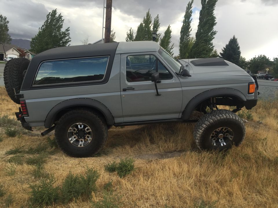 Gray lifted Ford Bronco with a spare tire on the back, parked on dry grass