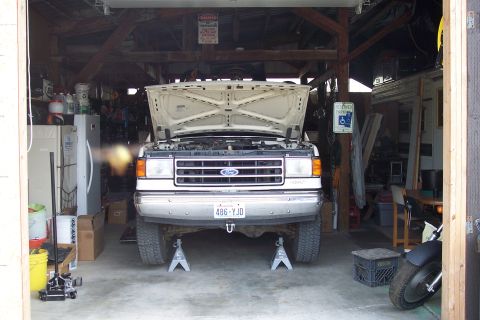 1990 Ford Bronco - A white 1990 Ford Bronco is parked in a garage with its hood open and front end raised on jack stands.