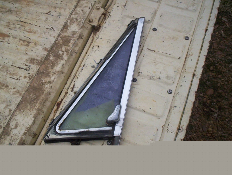 Removed chrome-framed vent window with latch lying on a rusty white truck bed