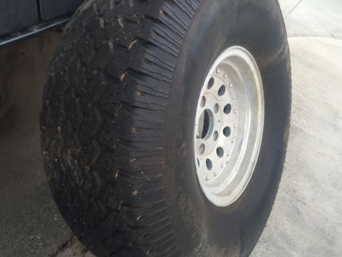 1986 Ford Bronco - A close-up view of a large off-road tire mounted on a silver multi-hole wheel.