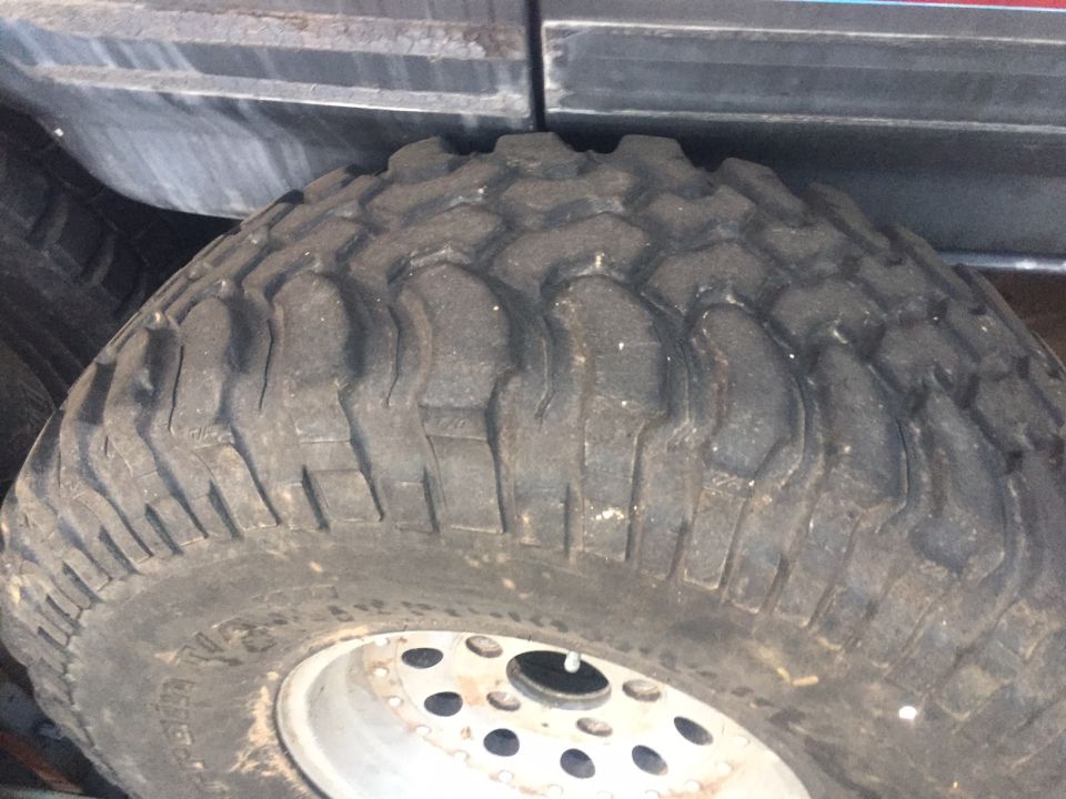 Close-up of a large off-road tire with aggressive tread pattern and a silver wheel with multiple lug holes