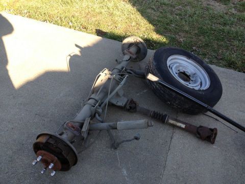 1995 Ford Bronco - A disassembled rear axle assembly and a spare tire lie on a concrete surface next to a grassy area.