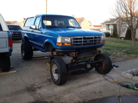 1995 Ford Bronco - A blue Ford Bronco is undergoing modifications, with its front end elevated for work on the suspension and chassis.