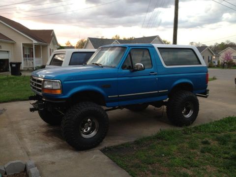 1995 Ford Bronco - A lifted 1992 Ford Bronco with a white removable top sits on a driveway next to another vehicle.