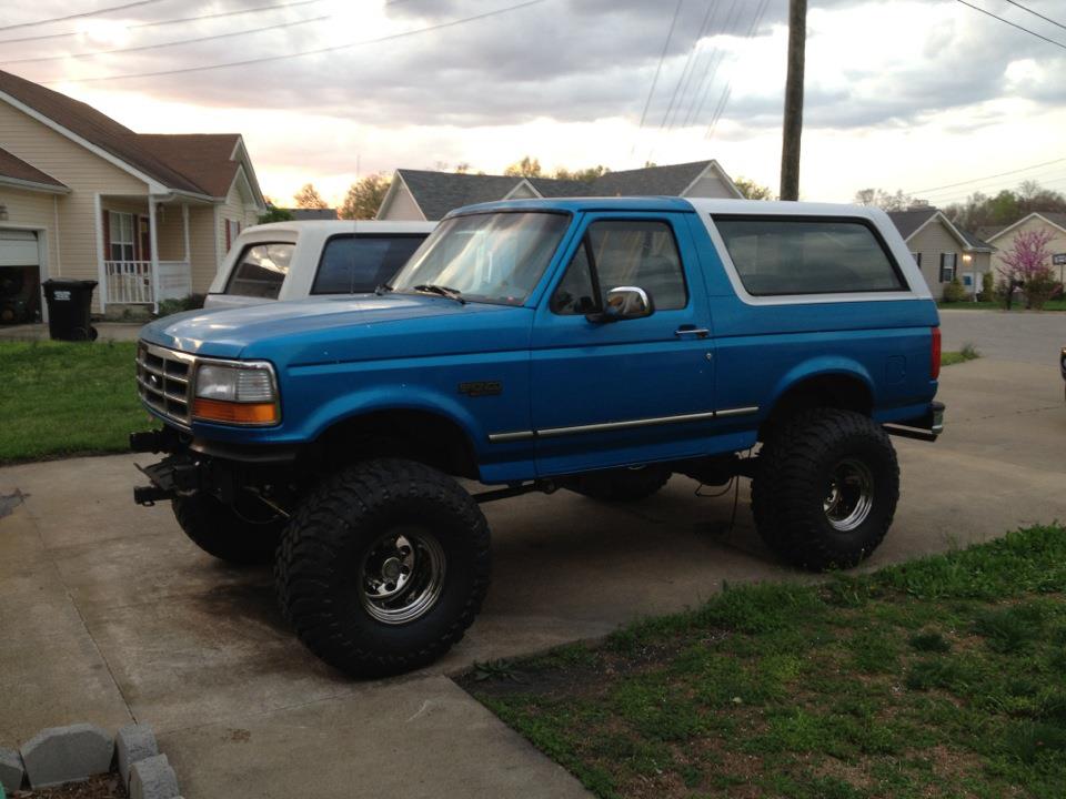Blue lifted 1992 Ford Bronco with white top, large tires, and aftermarket bumper