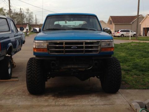 1995 Ford Bronco - A lifted blue 1995 Ford Bronco is shown from the front, parked next to another vehicle.