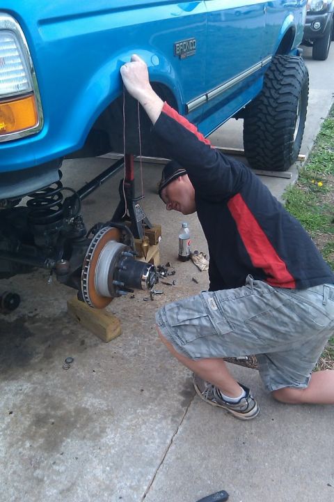 1995 Ford Bronco - A man works on the front wheel assembly of a blue 1995 Ford Bronco.