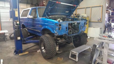 1995 Ford Bronco - A blue SUV is on a lift in a garage with its hood open and the front end partially disassembled.