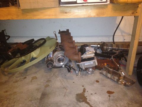 1995 Ford Bronco - Turbocharger and exhaust manifold parts are scattered on a concrete floor.