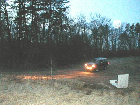 1995 Ford Bronco - A 1995 Ford Bronco is seen off-road at dusk, with its headlights illuminating the scene.