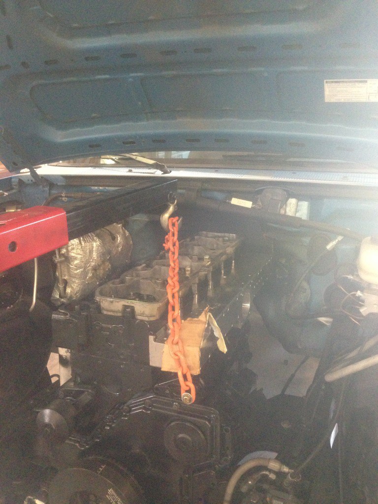 Engine bay with an orange chain lifting engine parts, under a blue hood