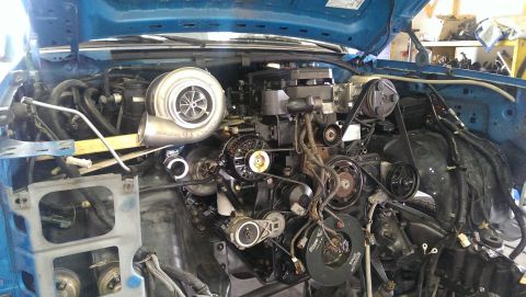 1995 Ford Bronco - The engine bay of a blue vehicle shows a large turbocharger and complex engine components.