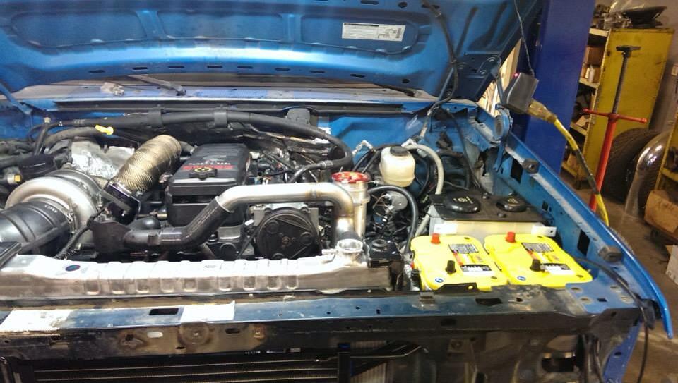 Blue truck engine bay with a large turbo and dual yellow batteries