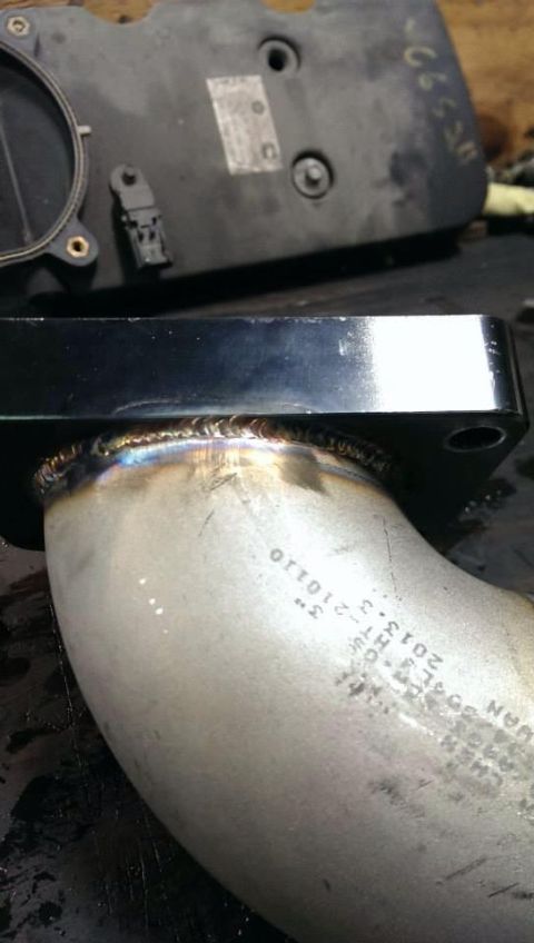1995 Ford Bronco - A close-up view of a custom-welded exhaust pipe and an engine part, with visible markings on the pipe.