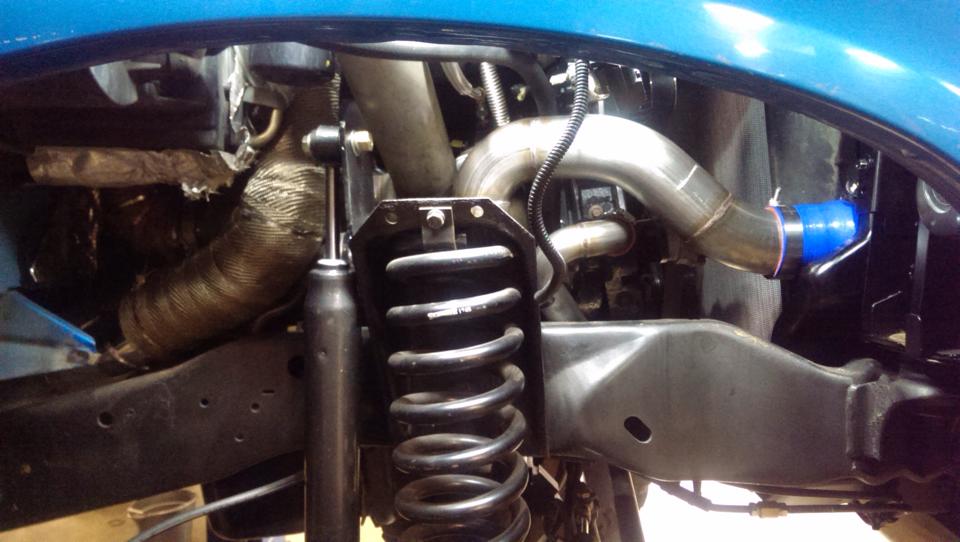 Close-up of exhaust piping, turbo piping with blue coupler, and suspension coilover in a vehicle's engine bay