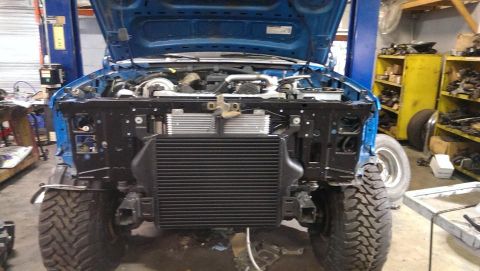 1995 Ford Bronco - Front view of a blue 1995 Ford Bronco with the hood open, revealing the engine and disassembled front end.