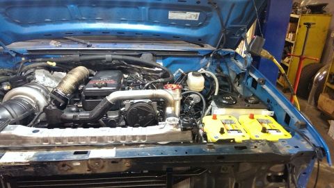 1995 Ford Bronco - The engine bay of a blue truck shows a large turbocharger and dual yellow batteries, indicating a custom build.
