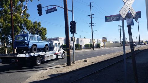 1973 Ford Bronco - A light blue, classic SUV is being transported on a flatbed tow truck on a sunny day. The SUV appears to be a Ford Bronco, with its rear en…