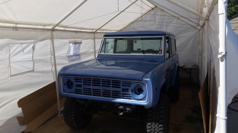 1973 Ford Bronco - A blue Ford Bronco is parked inside a white tent. The front of the vehicle is visible, showing its grille and headlights.