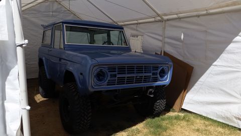 1973 Ford Bronco - A blue first-generation Ford Bronco is parked inside a white tent. The vehicle has large off-road tires and appears to be undergoing some r…