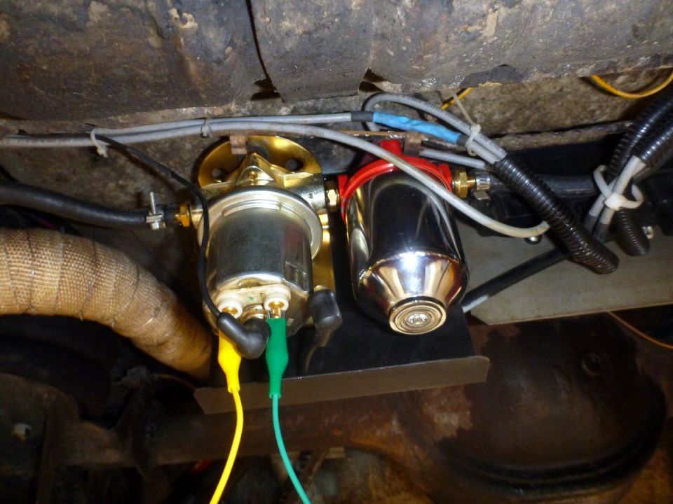 Chrome fuel filter with red top and attached electrical clips under a vehicle.