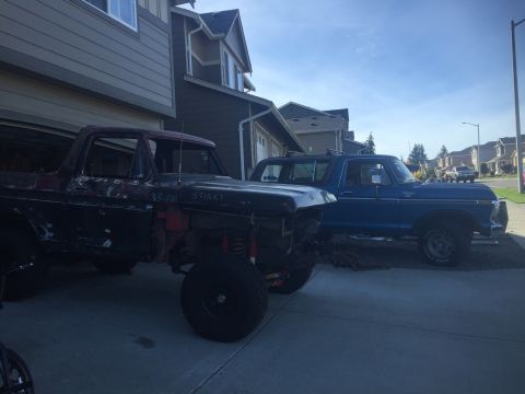 1978 Ford Bronco - A dark red, partially disassembled Ford Bronco is parked in front of a garage, with a blue Ford Bronco parked to its right. The dark red Br…