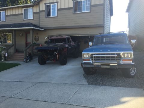 1978 Ford Bronco - A blue 1978 Ford Bronco is parked in a driveway in front of a house, next to a black off-road vehicle. The Bronco has a roof rack and large…