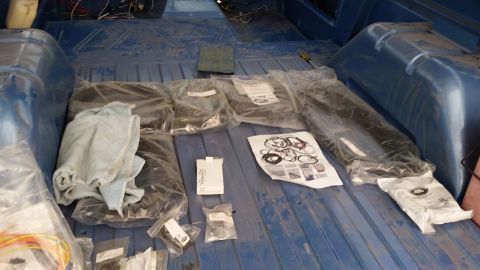 1973 Ford Bronco - The interior cargo area of a blue vehicle is filled with various parts and supplies, including several plastic-wrapped items, a folded towe…