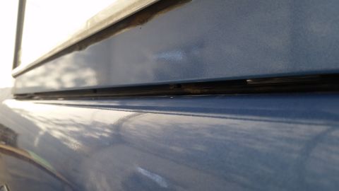 1973 Ford Bronco - A close-up, angled view of the blue painted body of a vehicle, showing a gap between two panels and a rubber seal.