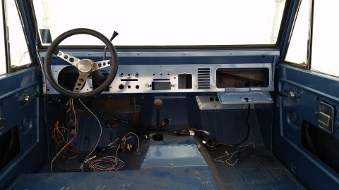1973 Ford Bronco - The interior of a classic Ford Bronco is shown, featuring a blue painted dashboard and floor. A steering wheel, shifter, and exposed wiring…