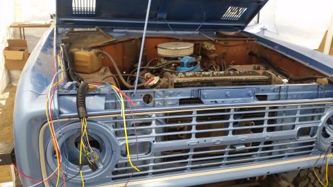 1973 Ford Bronco - The front end of a blue 1973 Ford Bronco is shown with the hood open, revealing the engine bay and a complex wiring harness running to the…