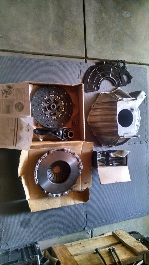 1985 Jeep CJ7 - A collection of clutch components and a bell housing are laid out on a gray mat on a concrete floor. The parts include two clutch discs, a…