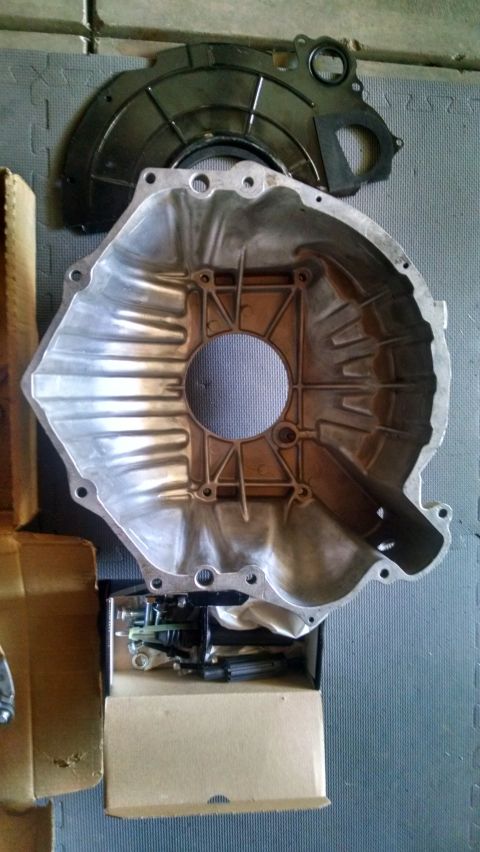 1985 Jeep CJ7 - A silver aluminum transmission bell housing and a black metal dust shield are laid out on a grey textured surface. A cardboard box containi…
