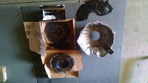 1985 Jeep CJ7 - A new clutch kit and transmission bell housing are laid out on a grey interlocking mat. The kit includes a clutch disc, pressure plate, and…
