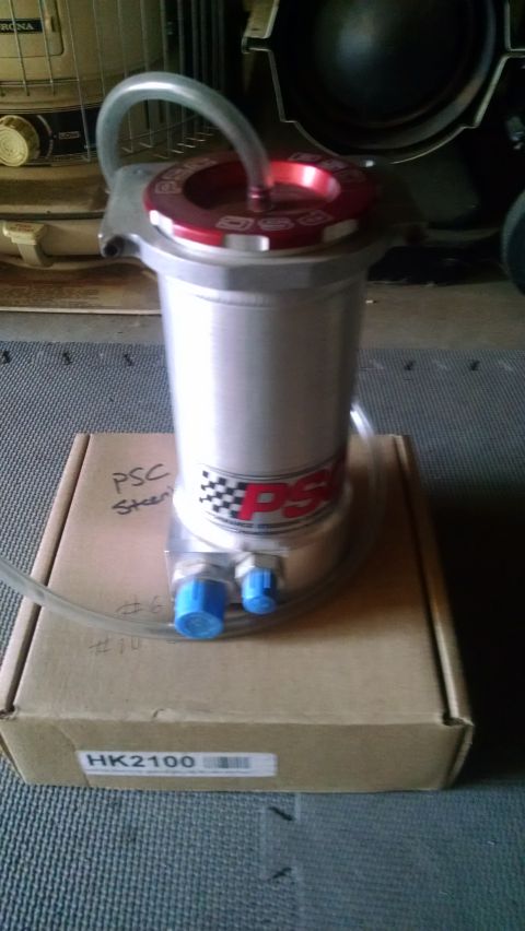 1985 Jeep CJ7 - A silver PSC power steering reservoir with a red cap sits on a cardboard box. The reservoir has blue fittings and a hose attached.