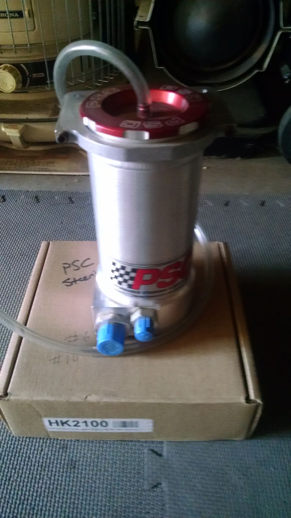 Silver PSC power steering reservoir with red cap and blue fittings.